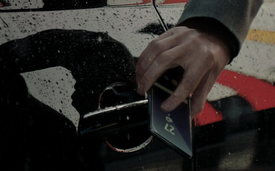 Close-up of a person unlocking a Genesis vehicle using a smartphone with Genesis Digital Key in rainy weather